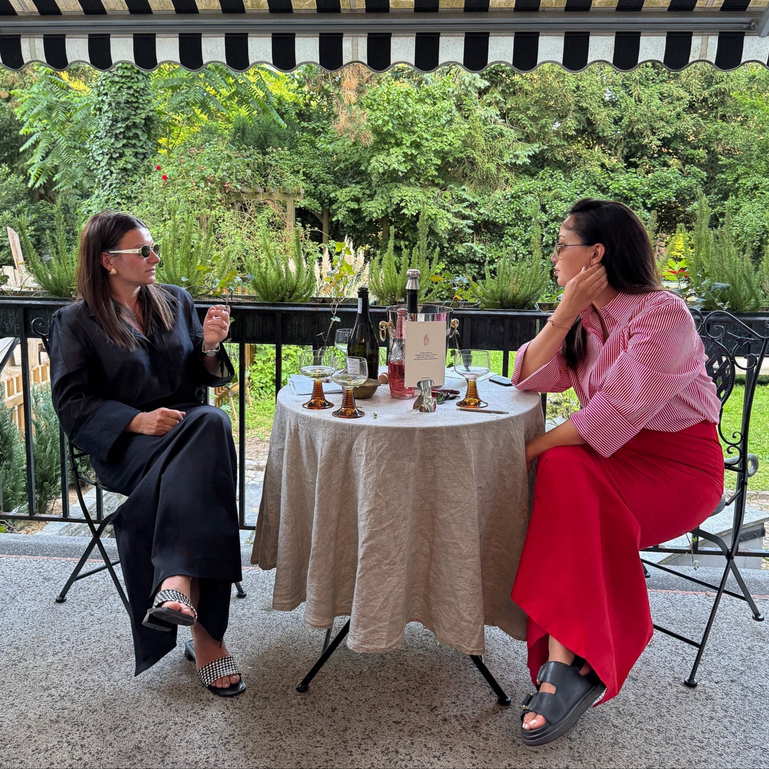Zwei Frauen im Gespräch auf der Terrasse des Ateliers von PALAIS du SOLEIL – entspannte Szene mit Blick ins Grüne, Teil des Brand-Launch Events der Kollektion The New Luxury
